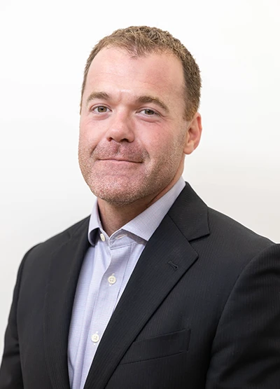 Portrait of Dr. Alex Kelamis wearing a black suit and light blue shirt